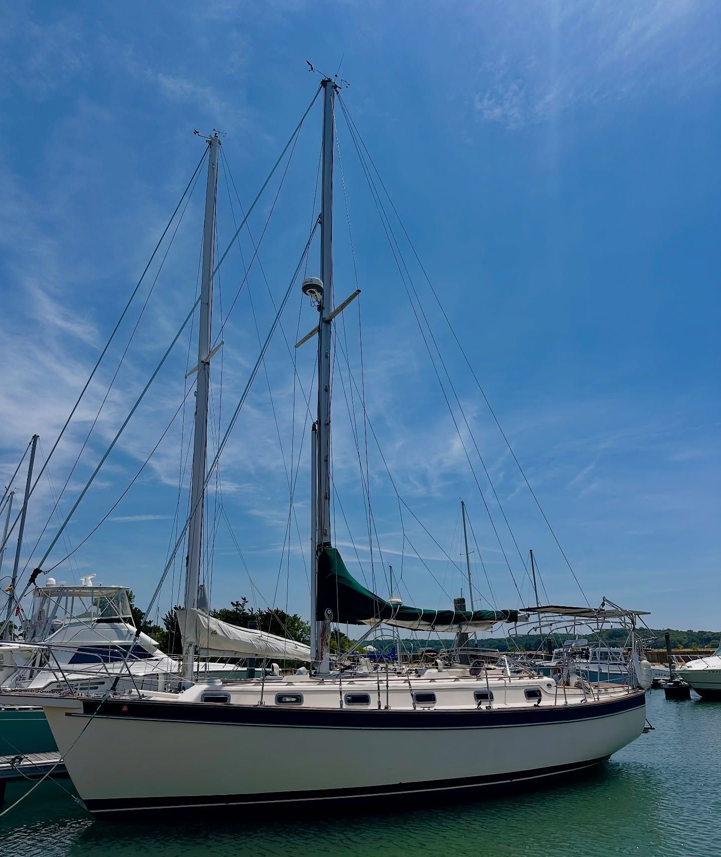 Sailboat docked in marina, blue sky, white hull, two masts.