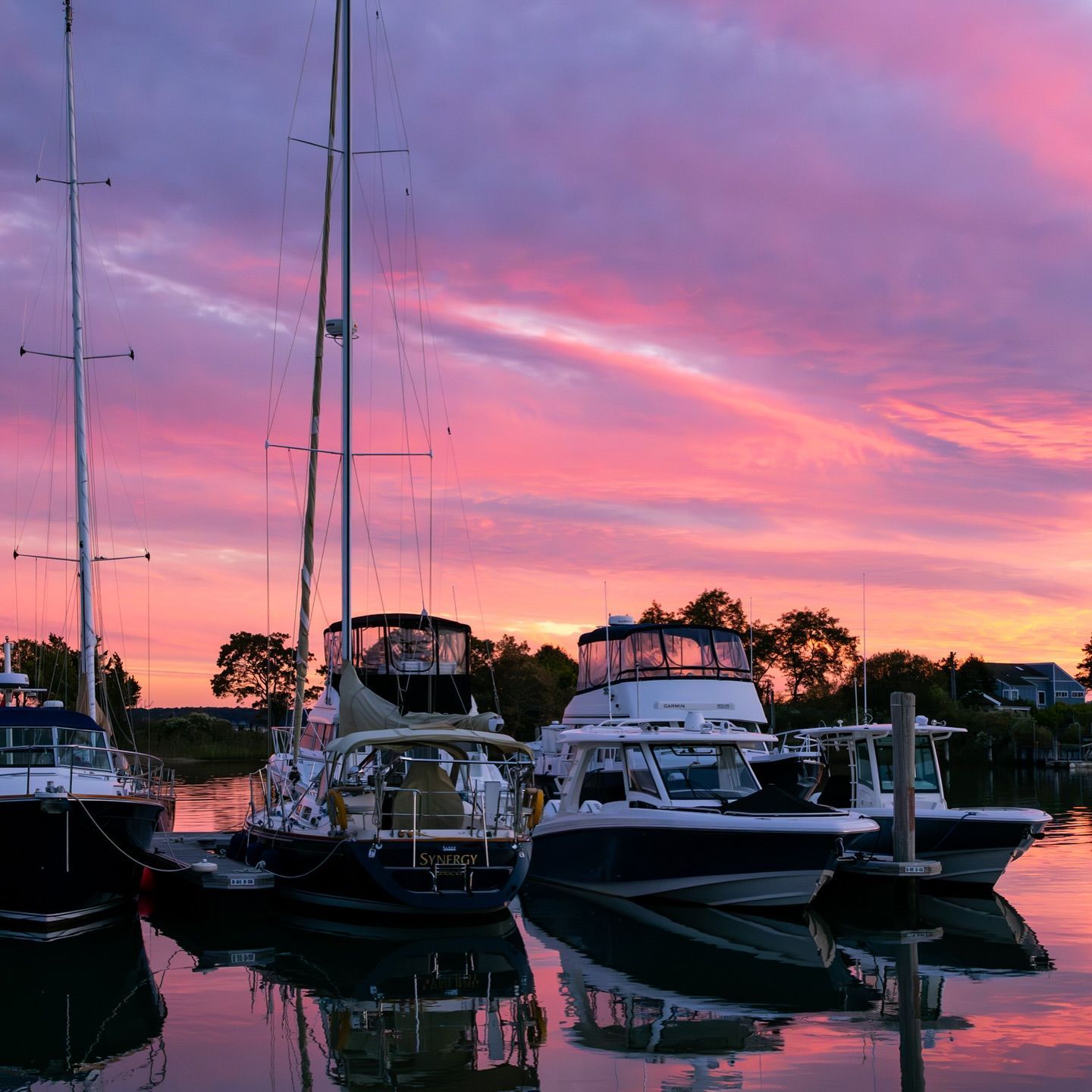 Boats docked at sunset, reflecting in calm water under pink and purple sky.