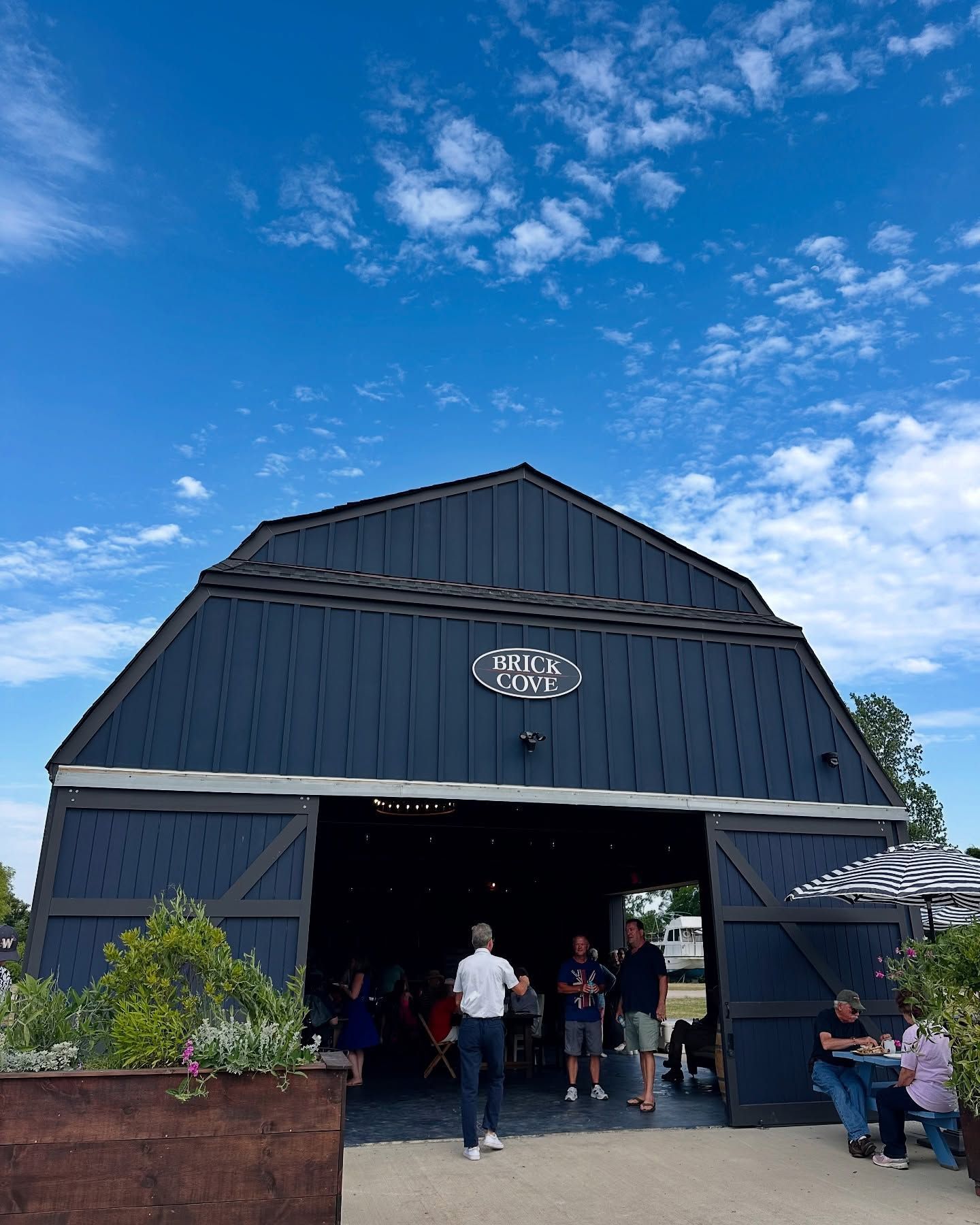 Dark blue barn with open doors; people inside, blue sky.