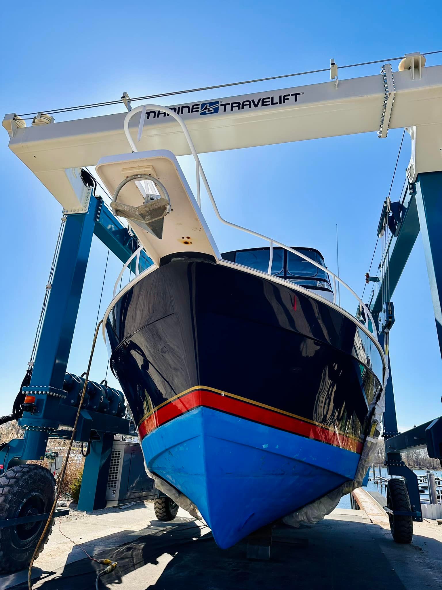 Blue boat suspended by a crane at a marina; blue sky overhead.