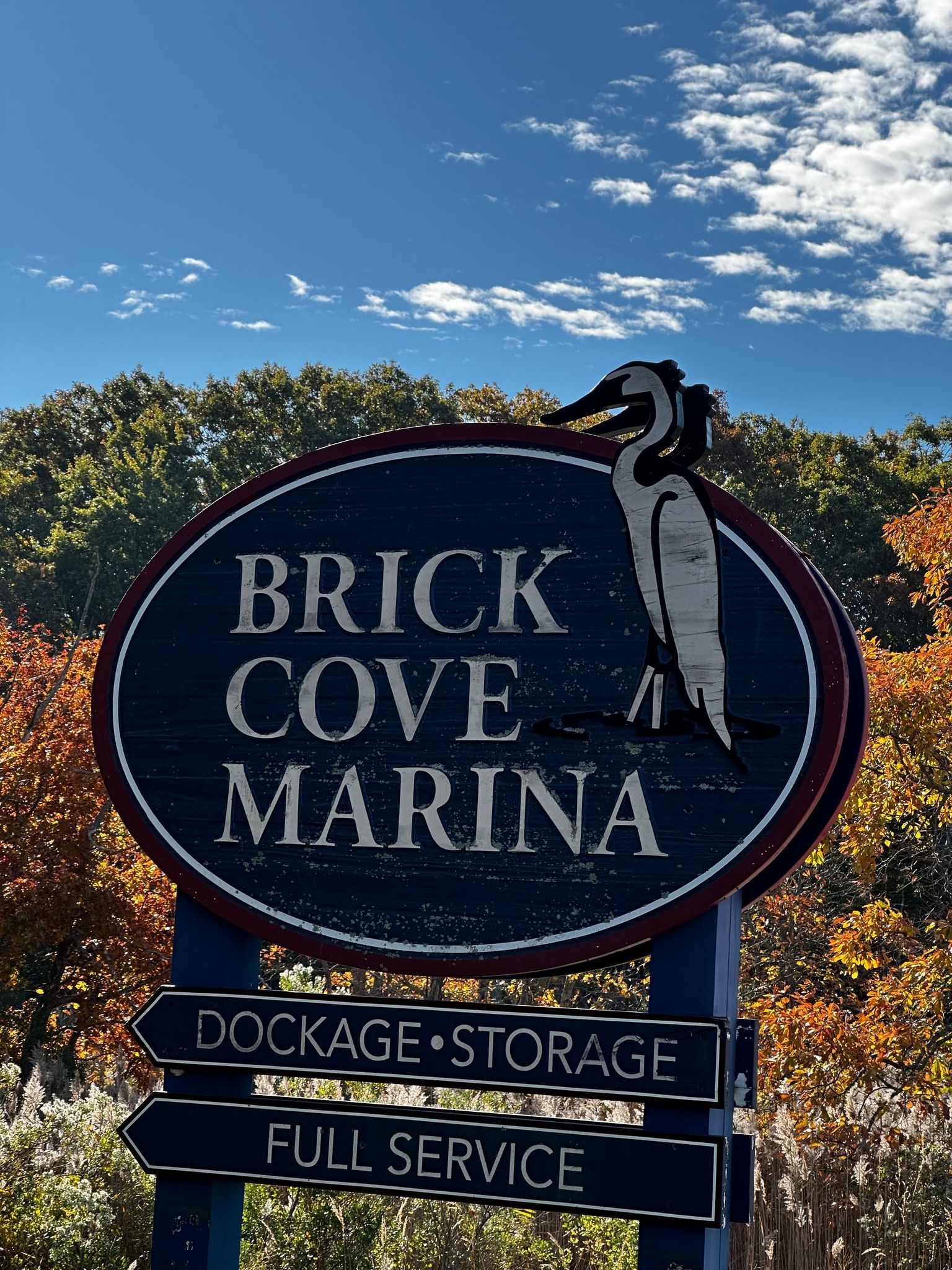 Sign for Brick Cove Marina with services listed; blue sky and trees in background.