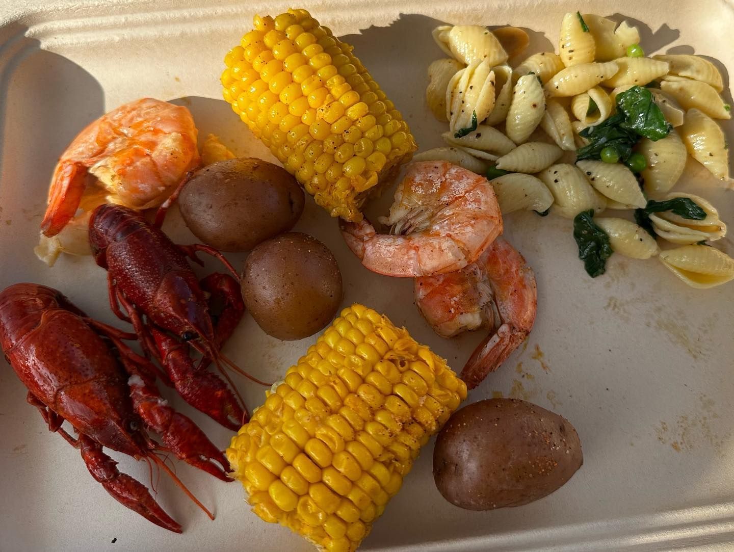 Shrimp boil with corn, potatoes, crawfish, and pasta in a white tray.