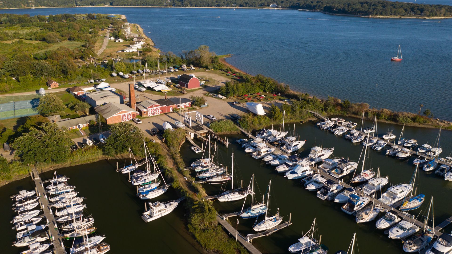 Aerial view of a marina with many sailboats docked, red buildings, and a blue sea.