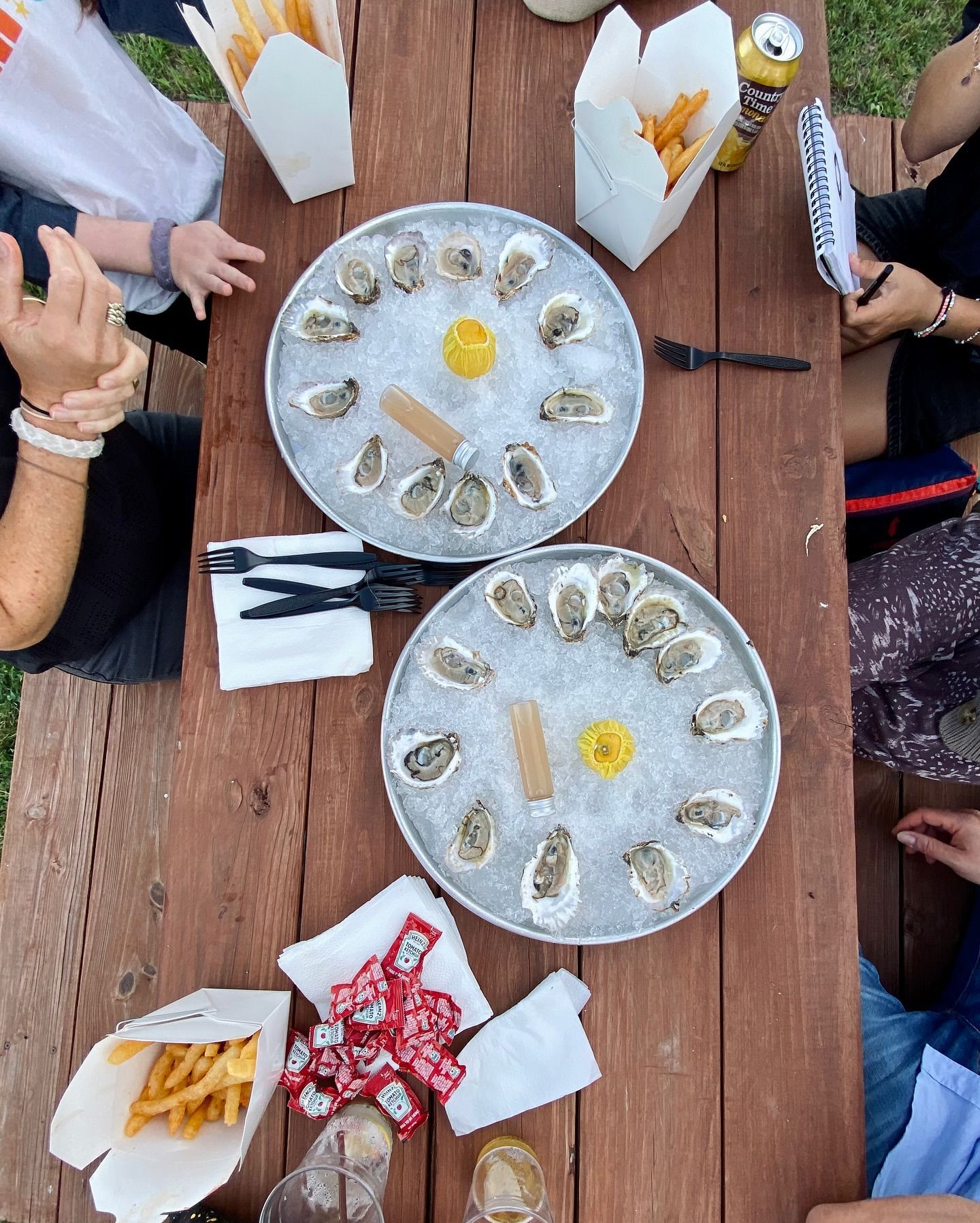 People at picnic table with oyster platters, fries, and drinks.