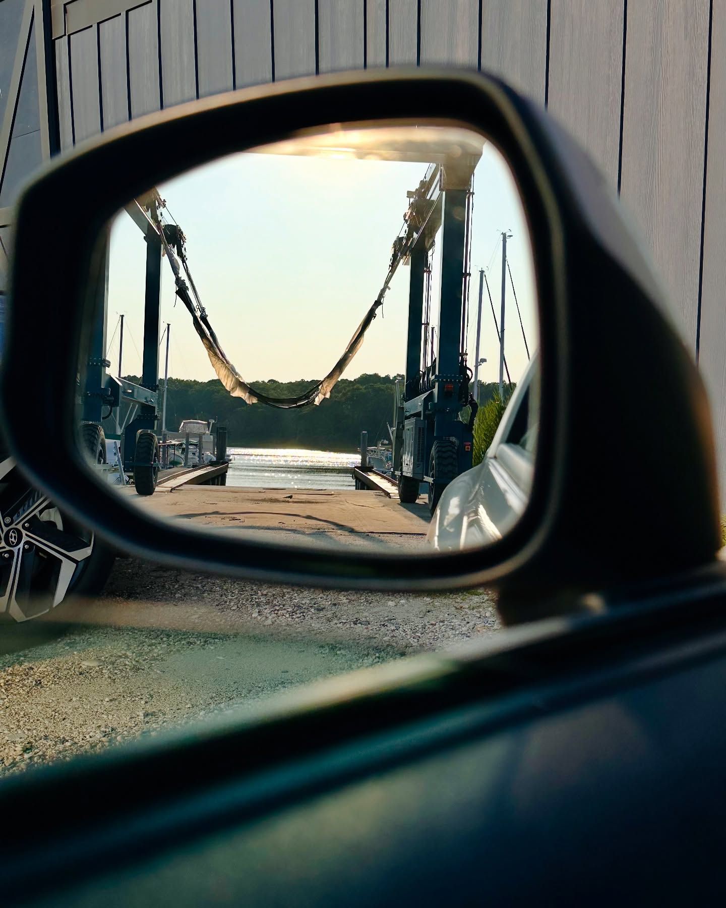 View in a side mirror of a car shows a ferry, bridge, and water.