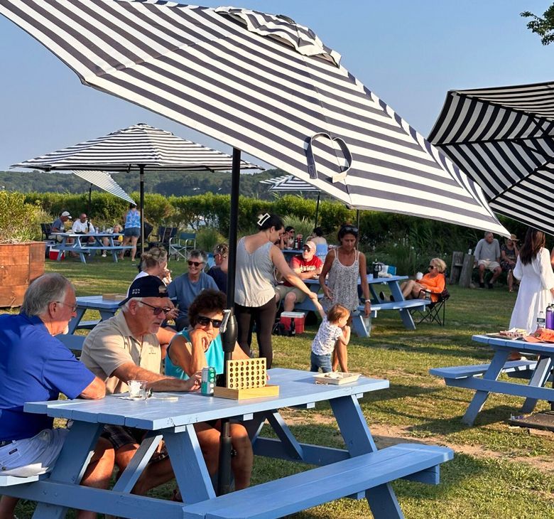 People picnicking at outdoor tables under striped umbrellas on a sunny day.