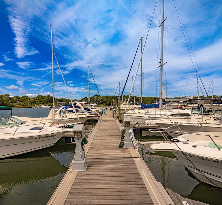 Boats docked at a wooden pier on a sunny day, blue sky with some clouds in the background.