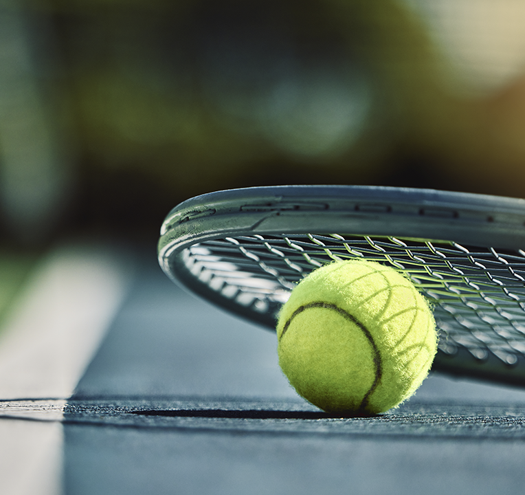 Tennis ball on court next to a tennis racket; green and black, blurred background.