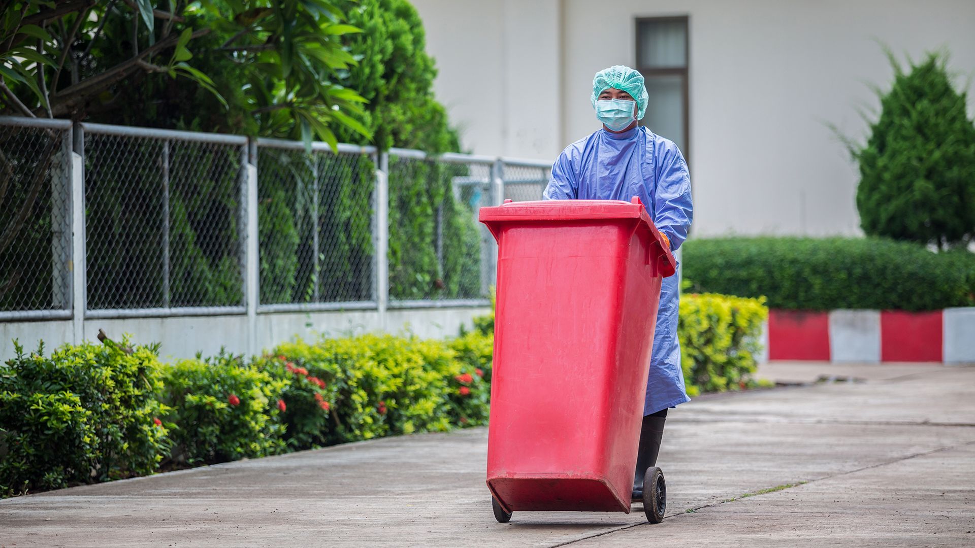 A medical worker pushing a red bin of medical waste outside