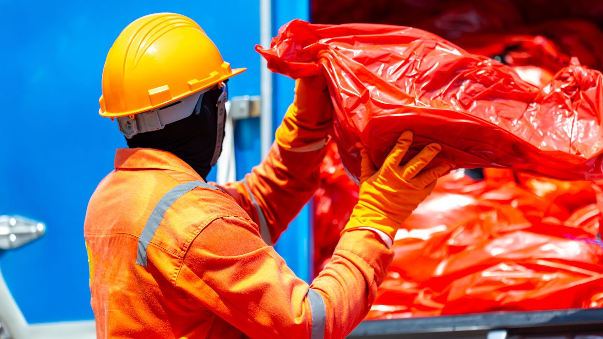 a hazardous waste disposal worker putting red trash bags into the back of a truck 