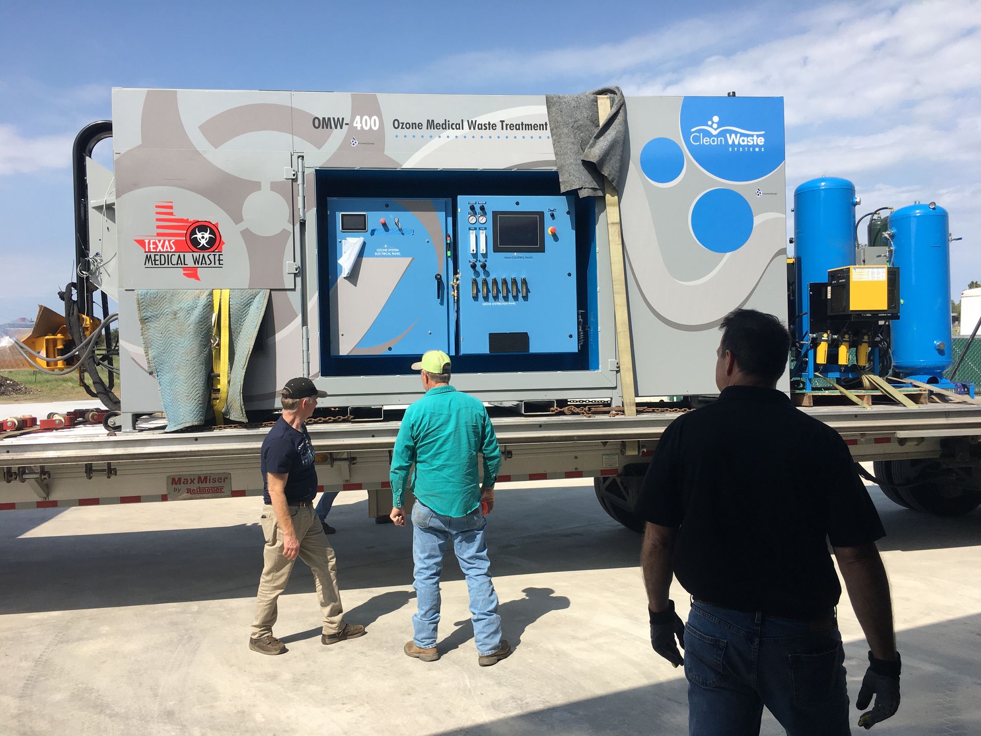 Three men are standing in front of a large machine on a trailer.
