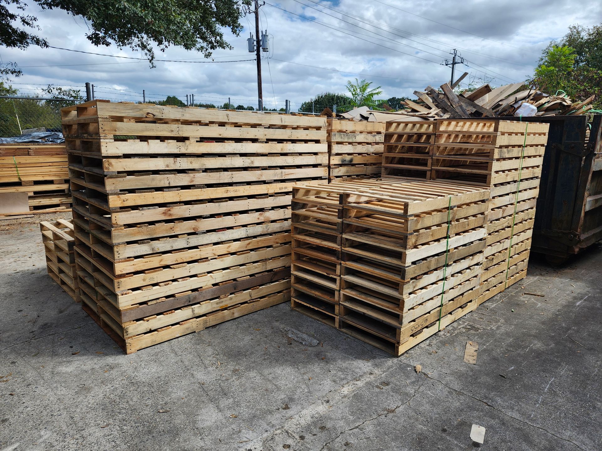 Stacks of wooden pallets in an outdoor setting. Various sizes and arrangements of wood. Gray concrete ground.
