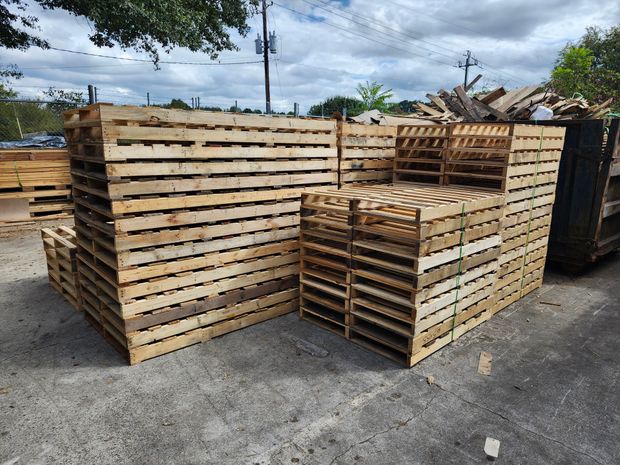 Stacks of wooden pallets in an outdoor setting. Various sizes and arrangements of wood. Gray concrete ground.