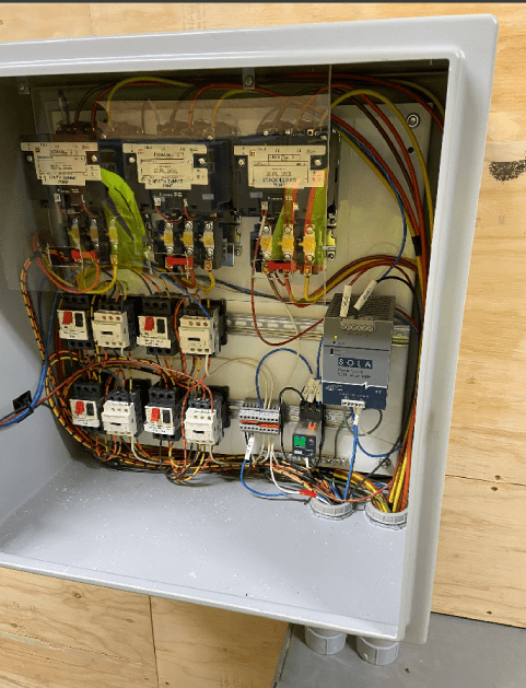 Electrical control panel with wires, circuit breakers, and relays inside a metal box.