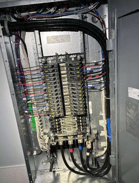 Electrical panel with wires, circuit breakers, and conduits in a metal cabinet.
