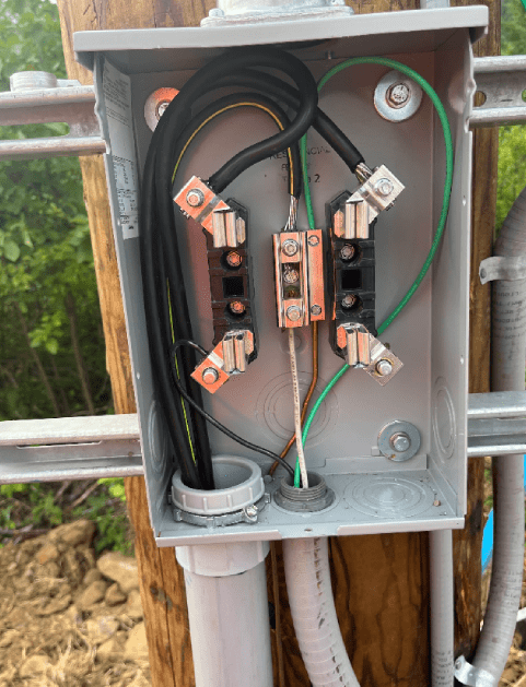 Electrical wiring in a metal box on a wooden pole, with black, green, and white wires connected.