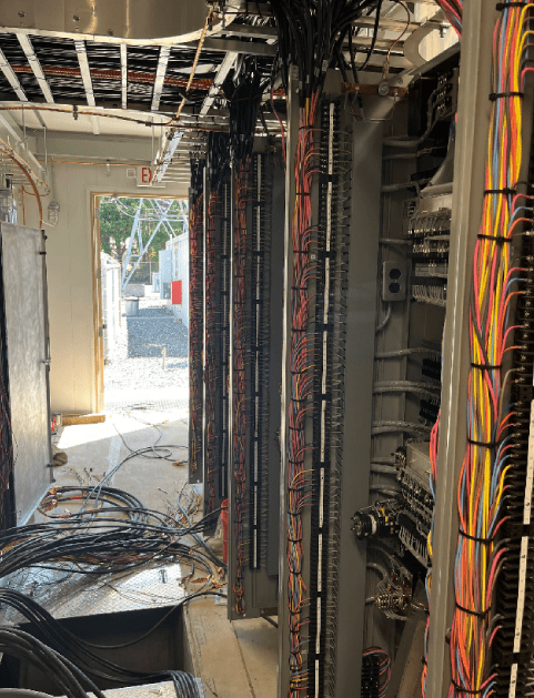 Electrical wiring in an unfinished room with open ceiling and vertical panels. Daylight visible at the doorway.
