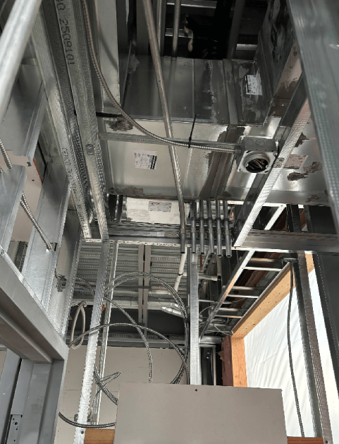 Interior view of a construction site ceiling, with metal framing, wires, and ventilation ducts.