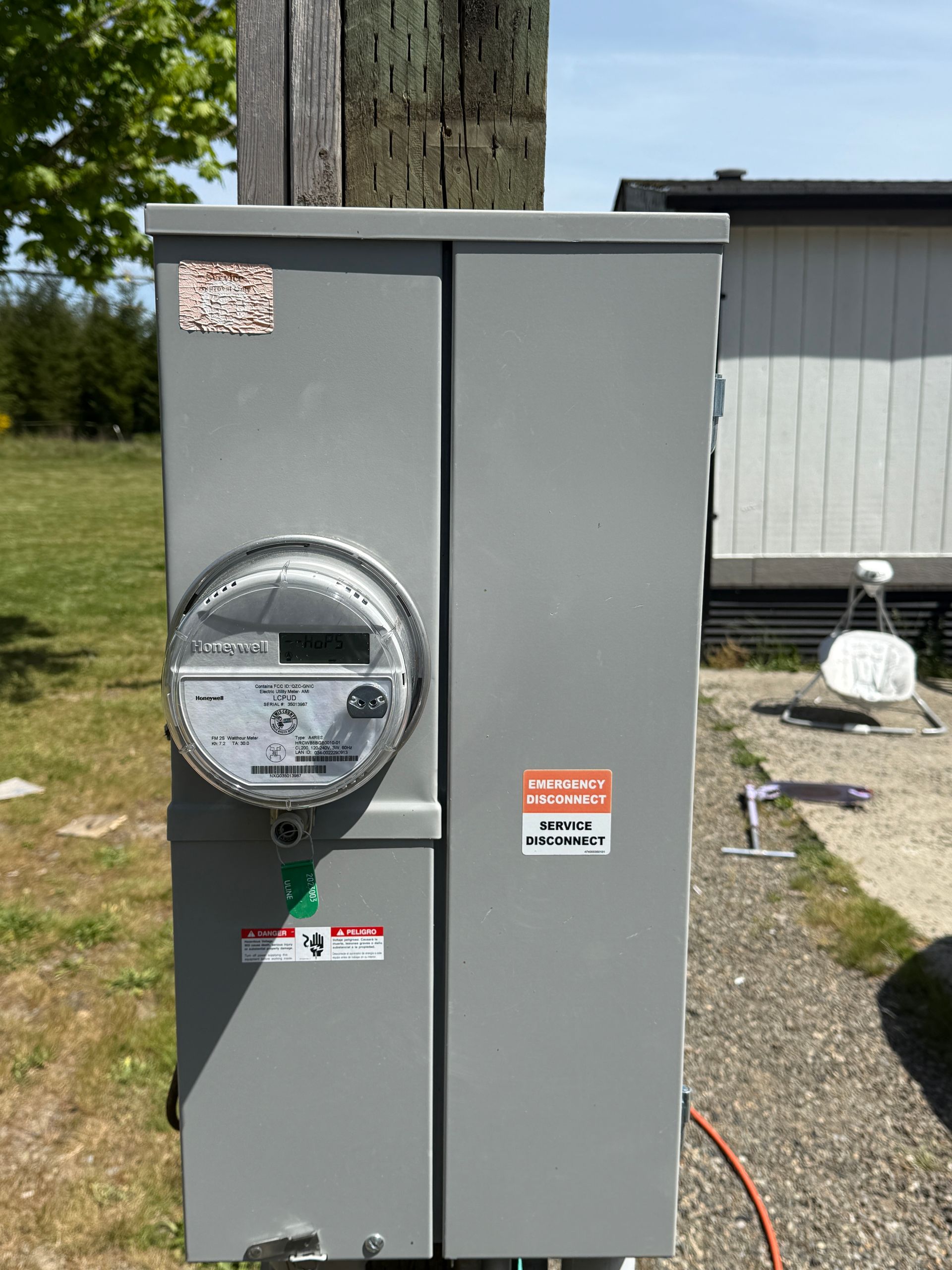 Electric meter and panel box mounted on a wooden utility pole, outdoors. Gray metal, with warning stickers.