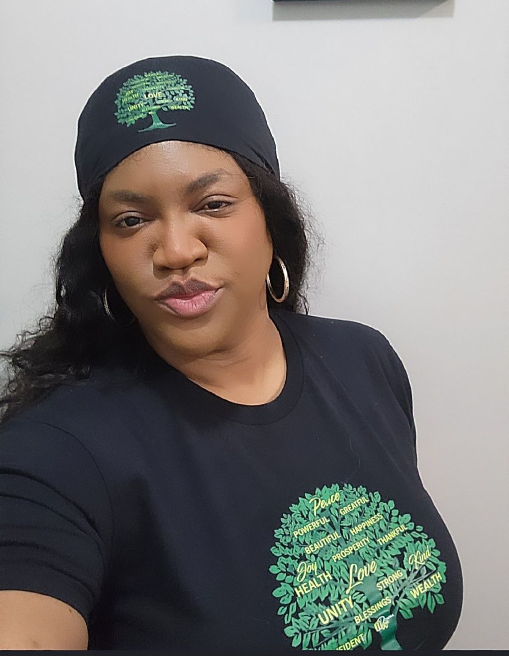A woman wearing a black hat and a black shirt with a green tree on it.