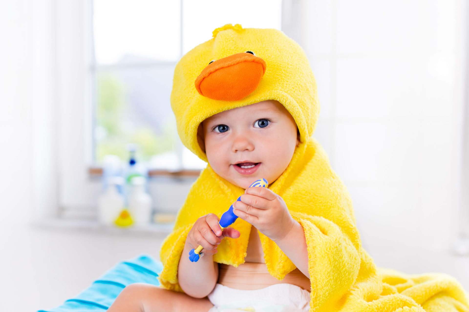 baby in yellow duck towel holding a toothbrush — kids dentist in Manalapan, NJ