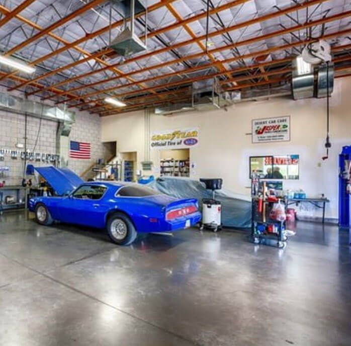 Blue classic car in a garage with tools, an American flag, and a Goodyear sign. | All Valley Car Care