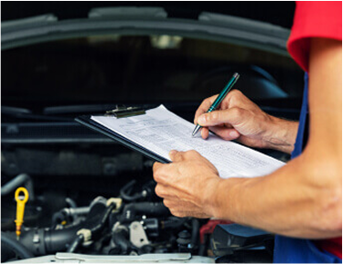 Mechanic inspects a car engine, writing on a clipboard. The engine is in the foreground, with the mechanic’s hands and torso visible. | All Valley Car Care