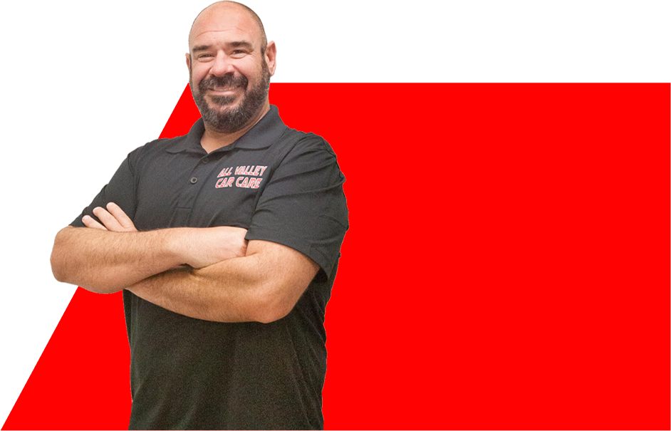 Man with crossed arms smiles in front of red and white background; shirt reads 