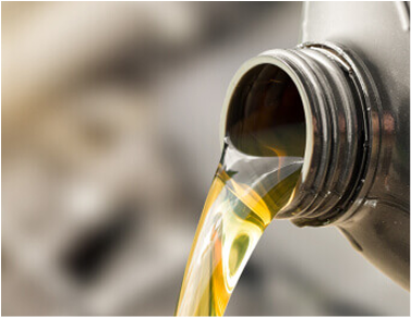 Oil pouring from a black bottle with a yellow-green color, in front of a blurred background. | All Valley Car Care