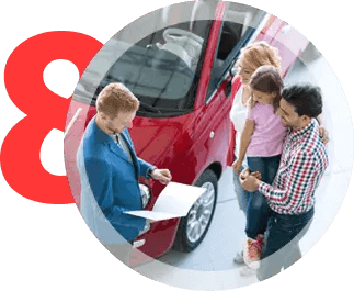 A car salesman showing paperwork to a family next to a red car in a dealership. | All Valley Car Care