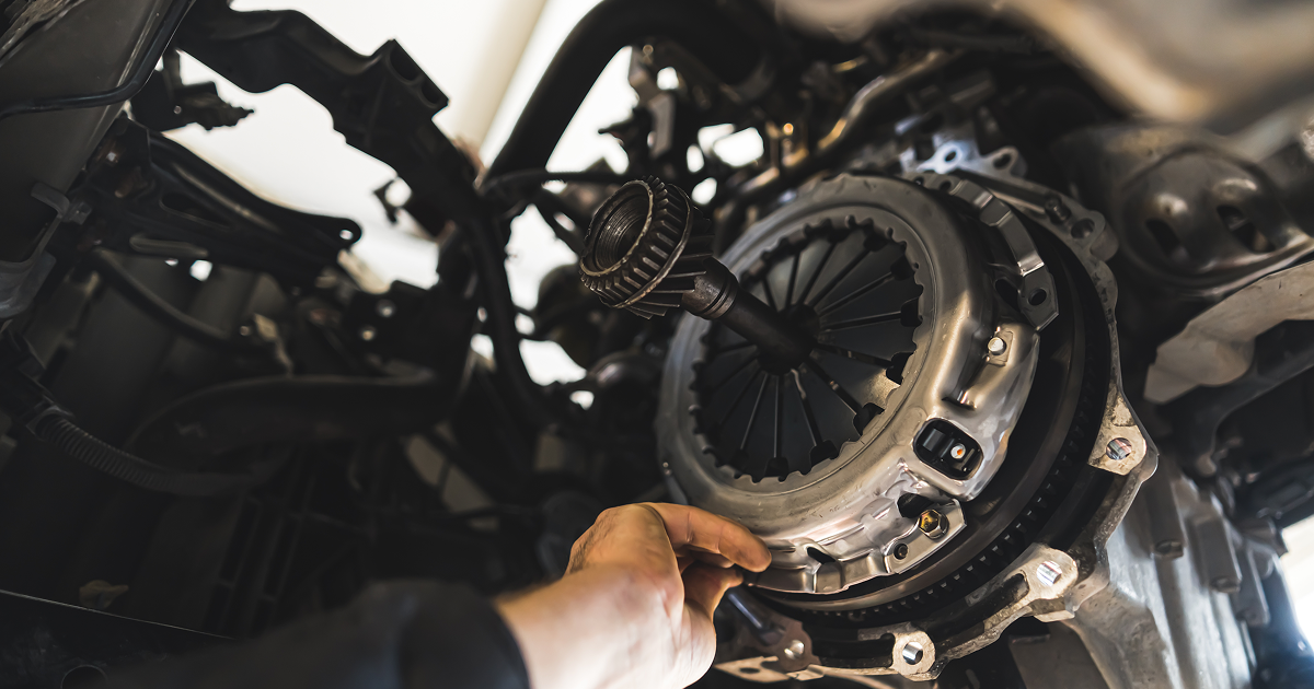 Hand working on a car's clutch system, possibly a repair. | All Valley Car Care