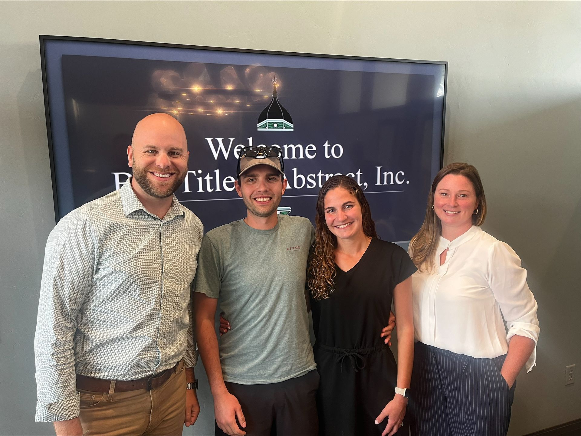 A group of people are posing for a picture in front of a sign that says welcome to little abstract inc.