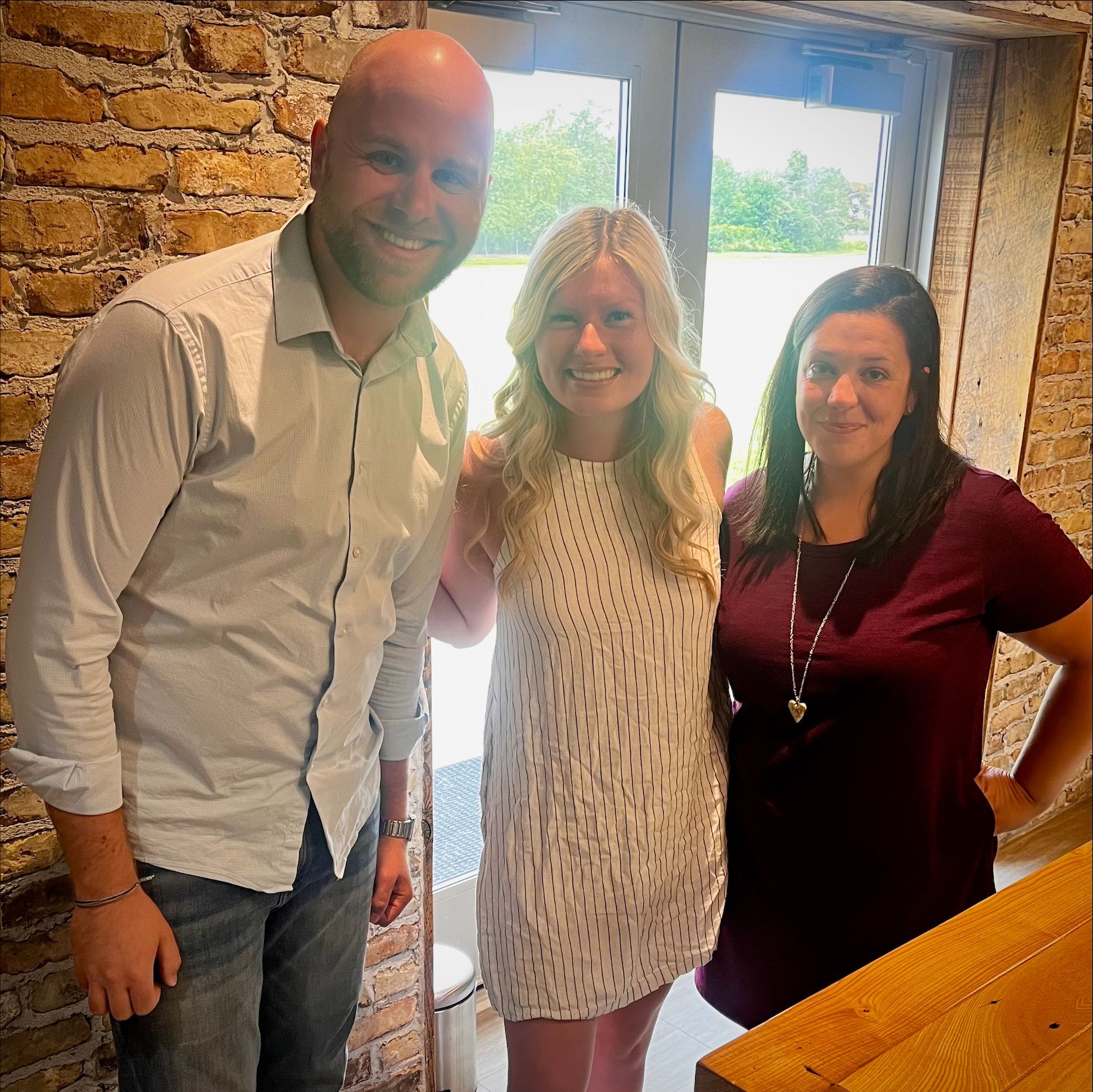 Three people posing for a picture in front of a brick wall