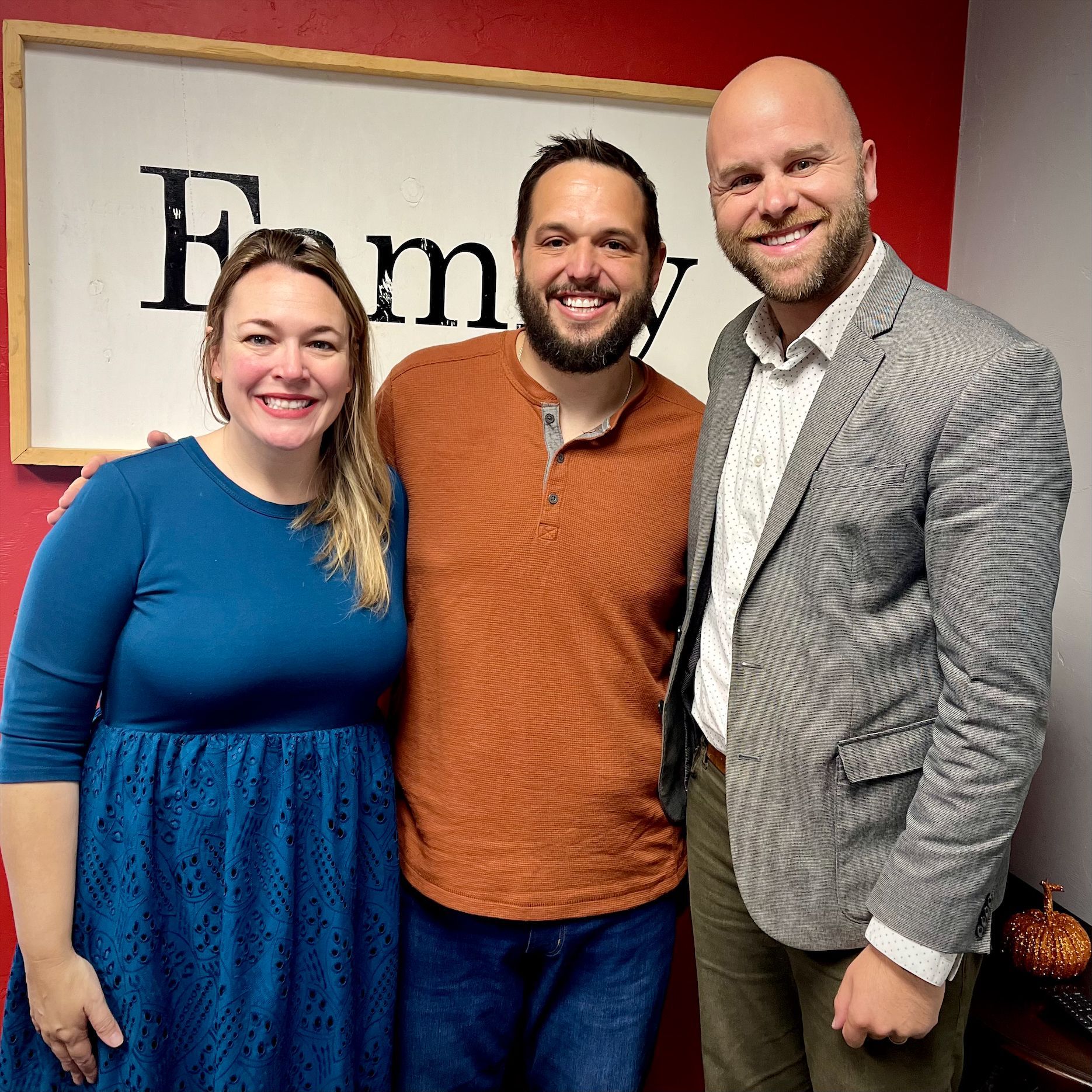 Three people are posing for a picture in front of a sign that says family