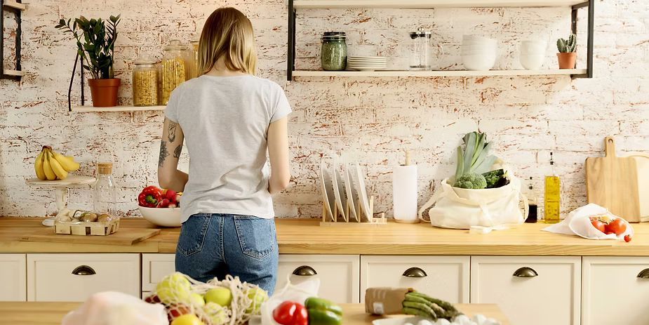 Woman in a kitchen, preparing food. Vegetables and fruit are on the counter.