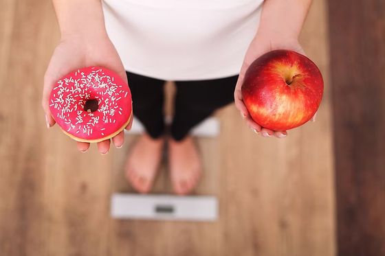 Person on scale holding a pink donut and red apple, representing food choice.