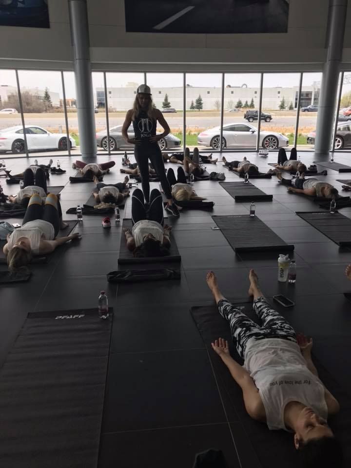 Group yoga class in a modern space with instructor. Participants on mats. Cars visible through large windows.