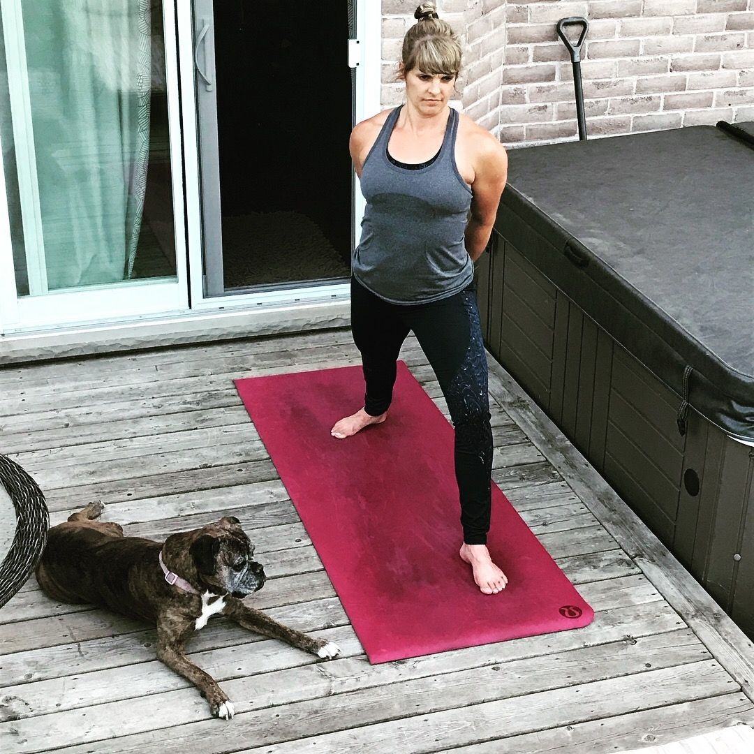 Woman in yoga pose on red mat, dog lying on wooden deck, back patio.