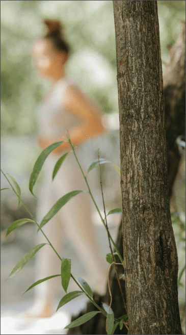 Woman in white dress near tree, natural light; green foliage.
