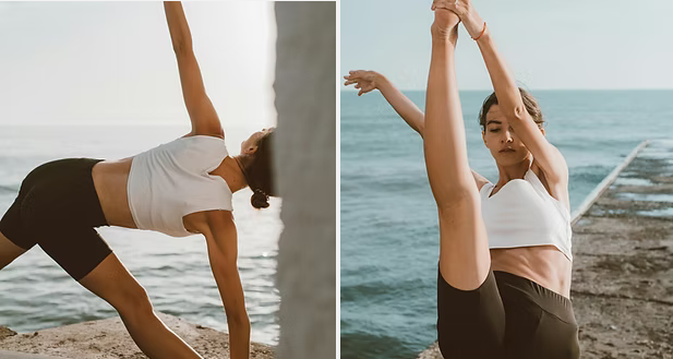 Woman doing yoga poses near the ocean, wearing white crop top and black shorts.