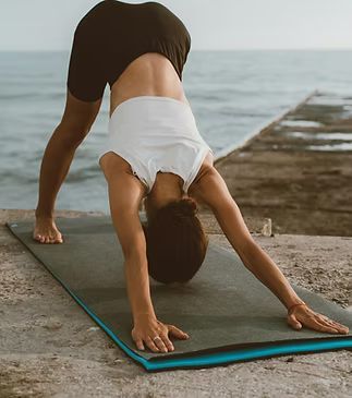Person in downward-facing dog pose on a yoga mat, outdoors by water.