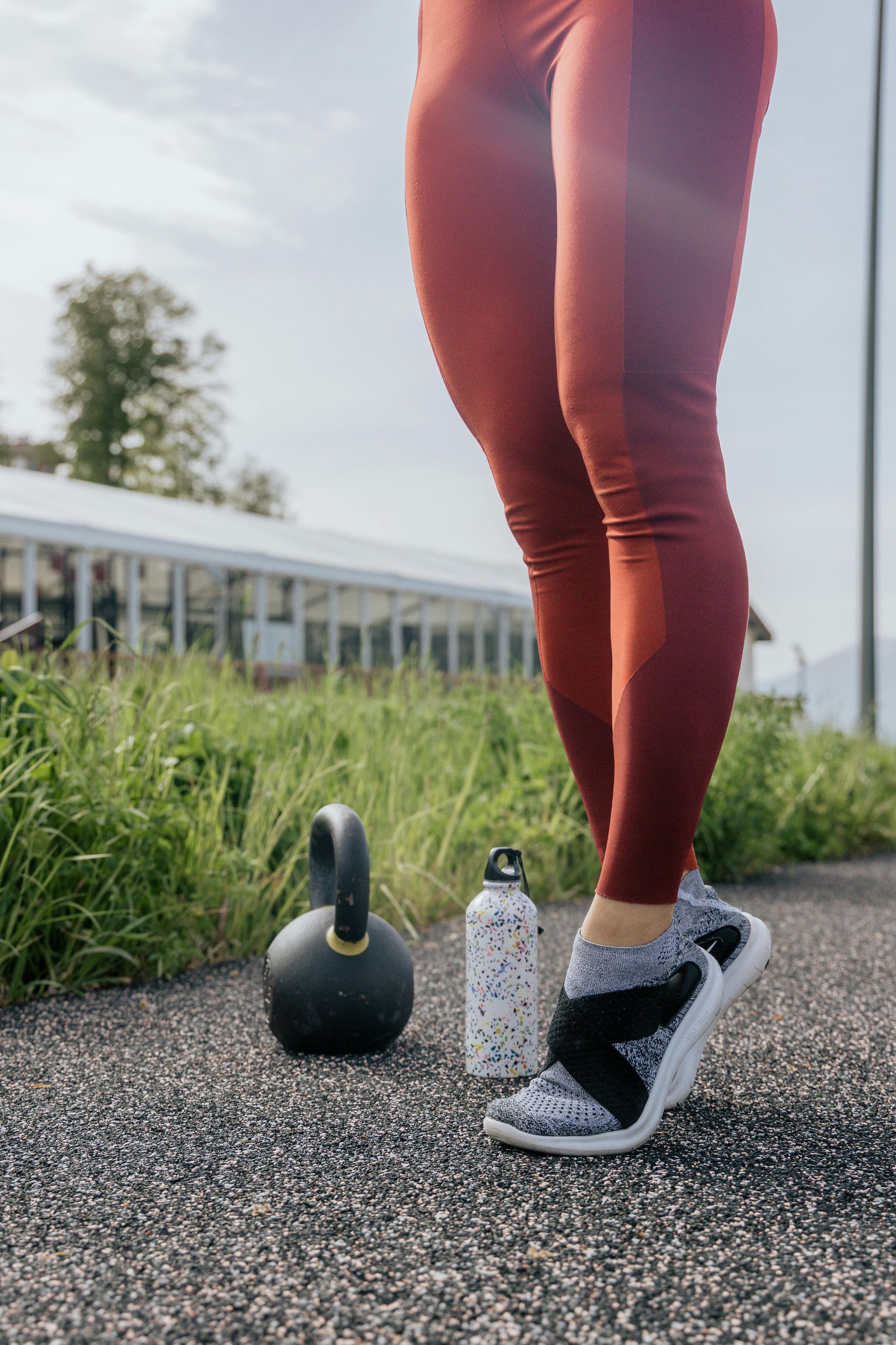 Person in red leggings near kettlebell and water bottle, outdoors.