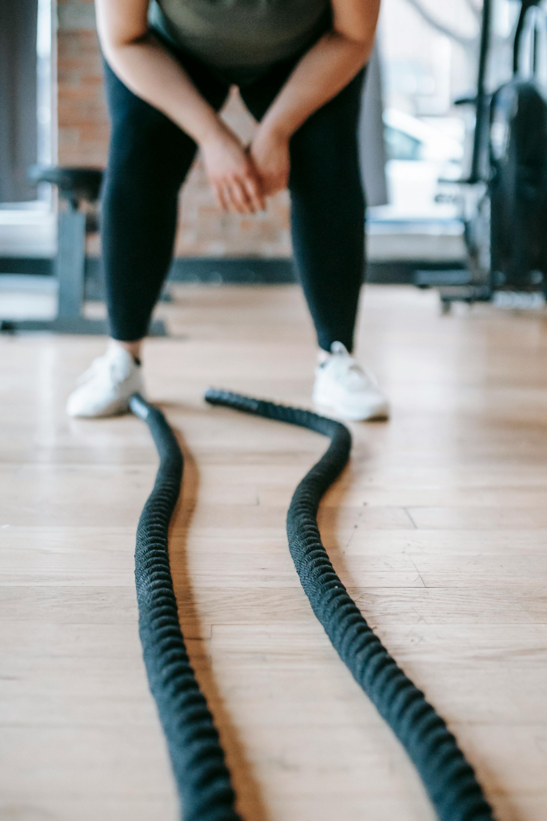 Person in gym with black ropes, wearing leggings and white sneakers.