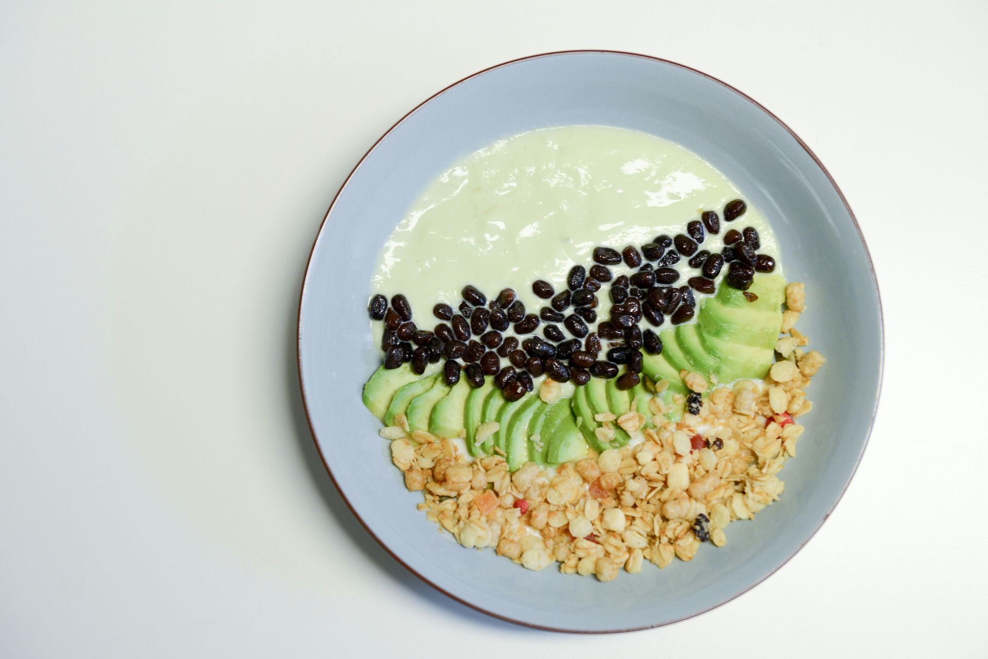 Blue bowl with green sauce, black beans, sliced avocado, and grain.