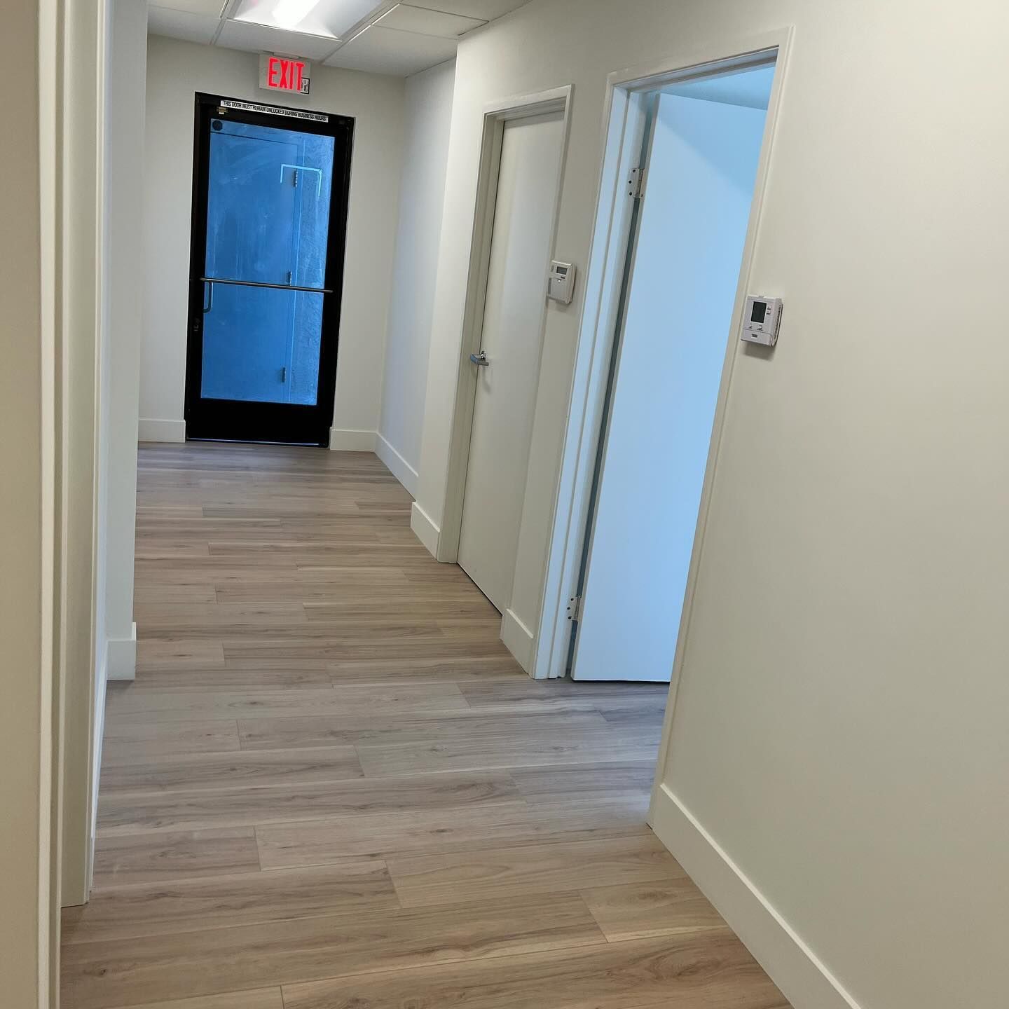 A hallway with a glass door and a red exit sign