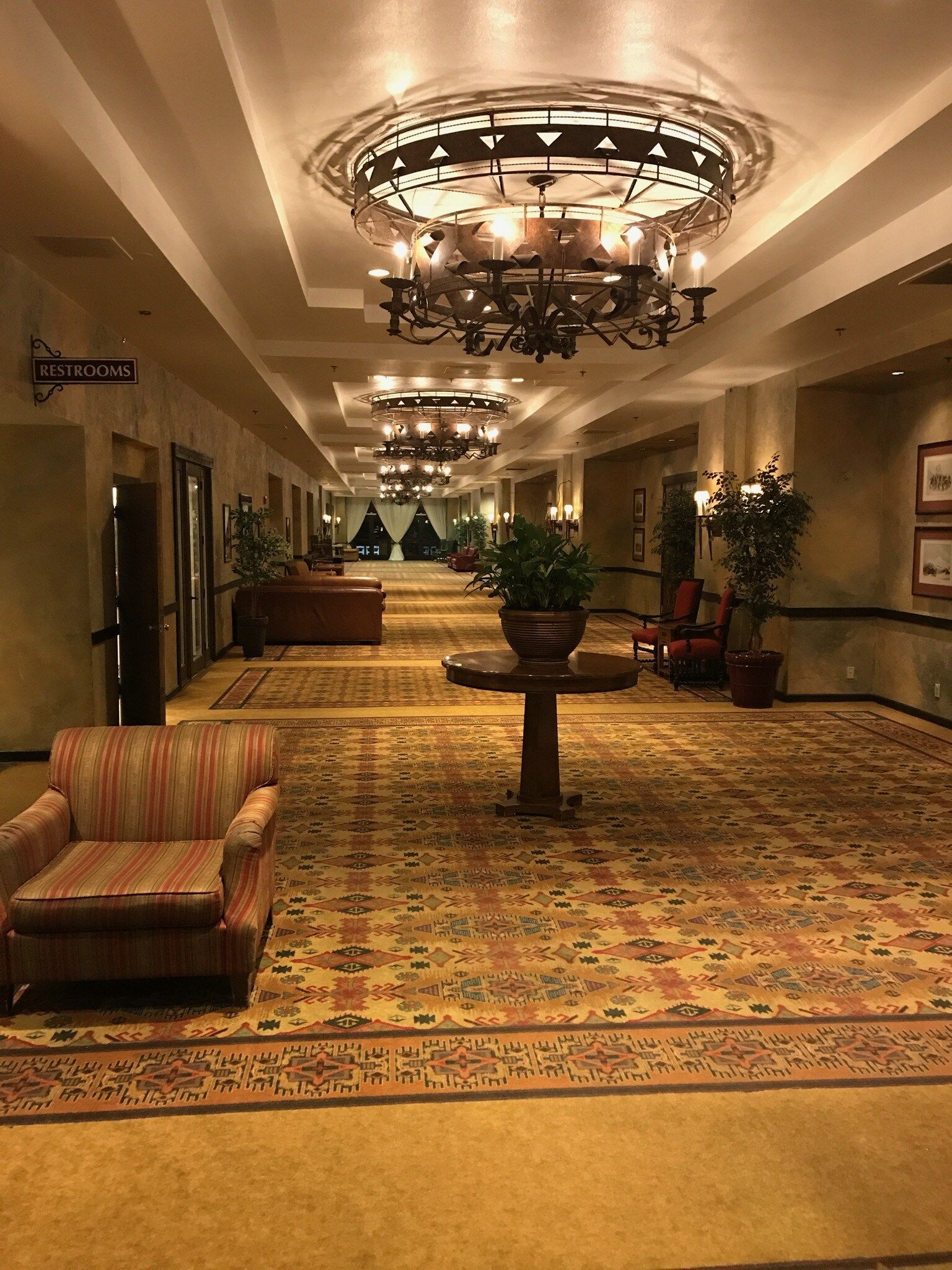 A long hallway with chairs , a table and a chandelier.