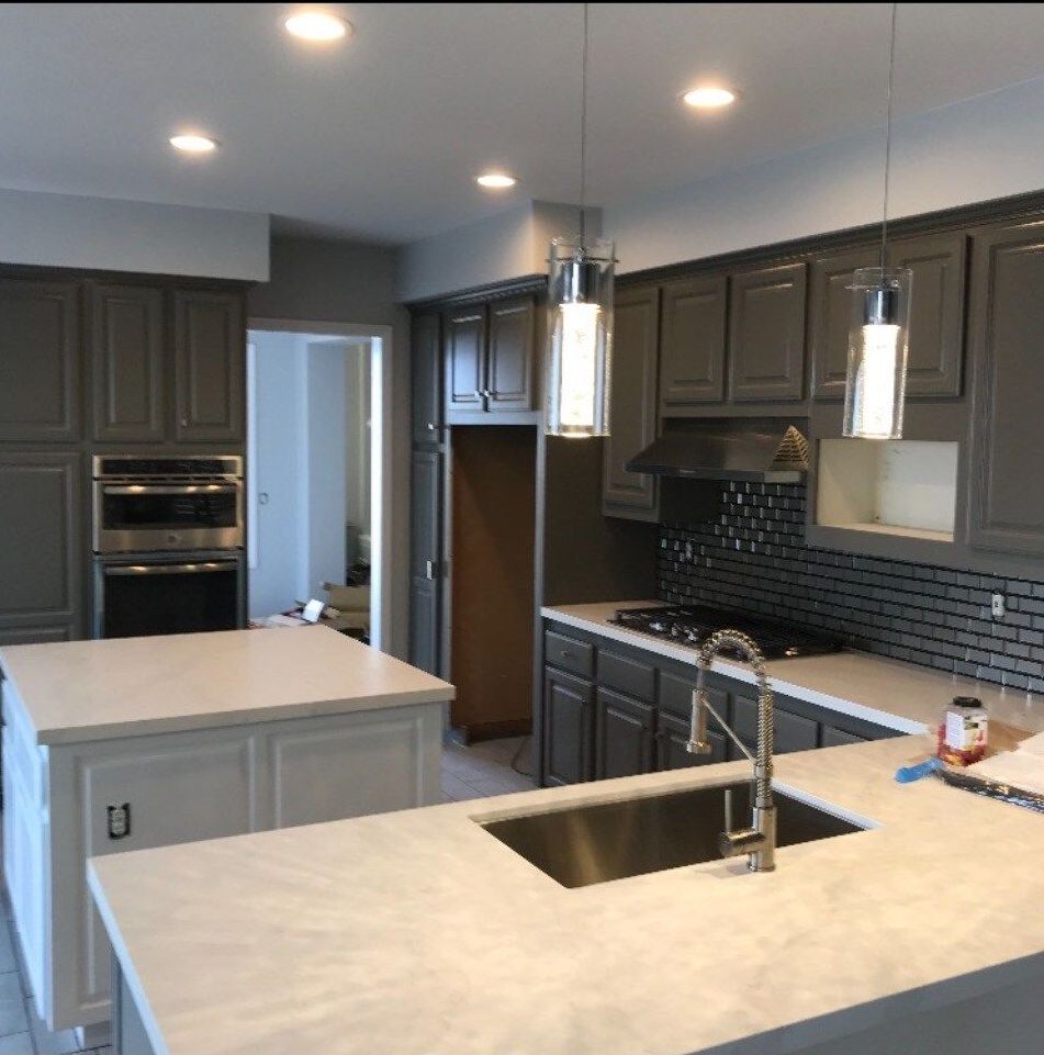 A kitchen with gray cabinets and white counter tops