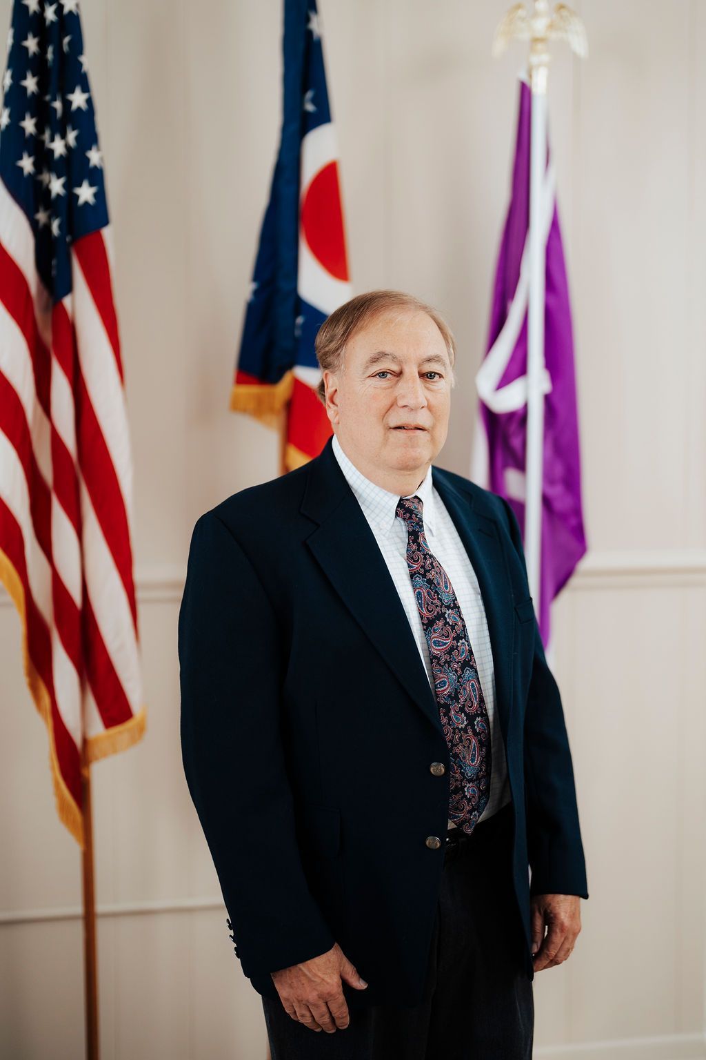 A man in a suit and tie is standing in front of flags.