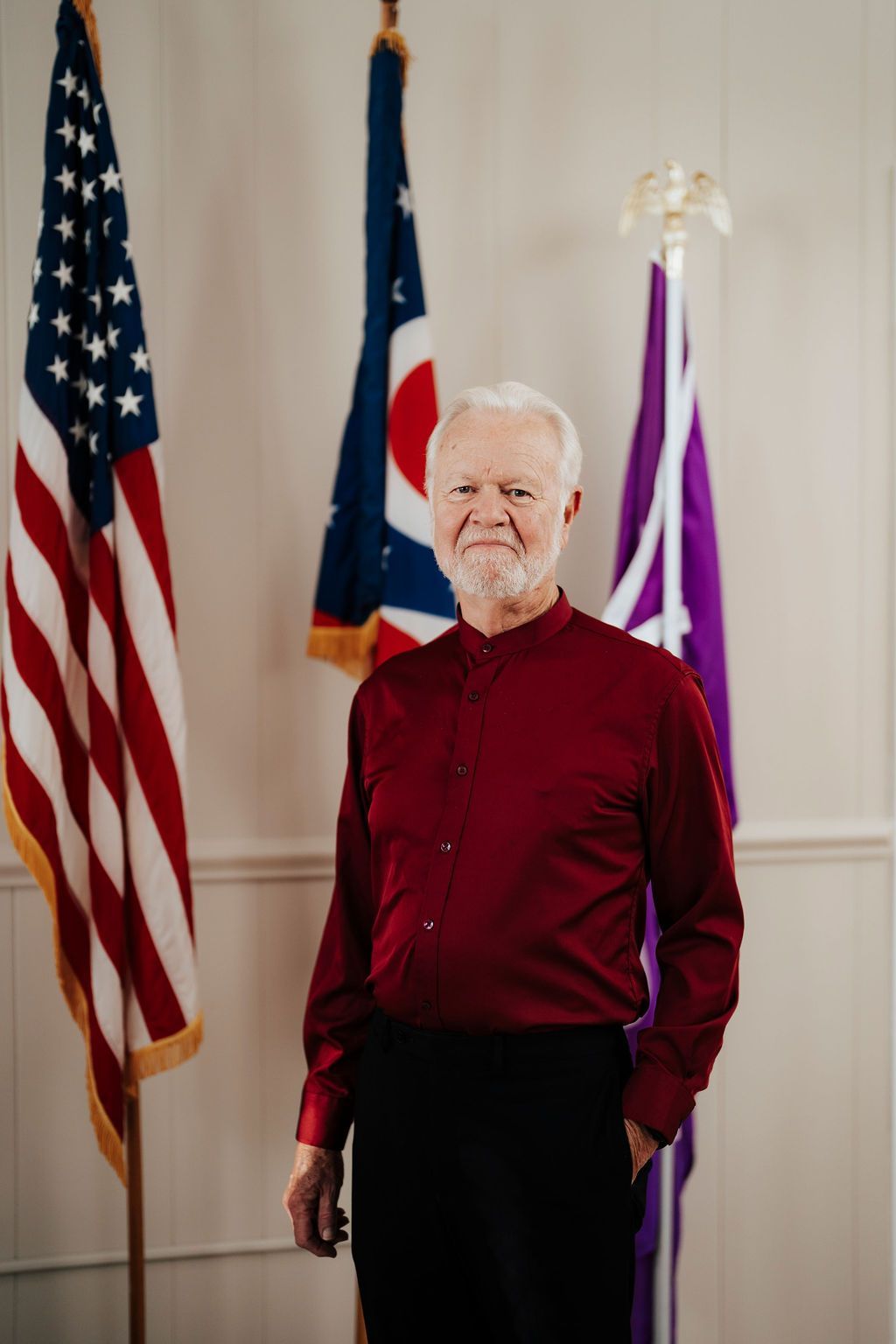 A man in a red shirt is standing in front of three flags.