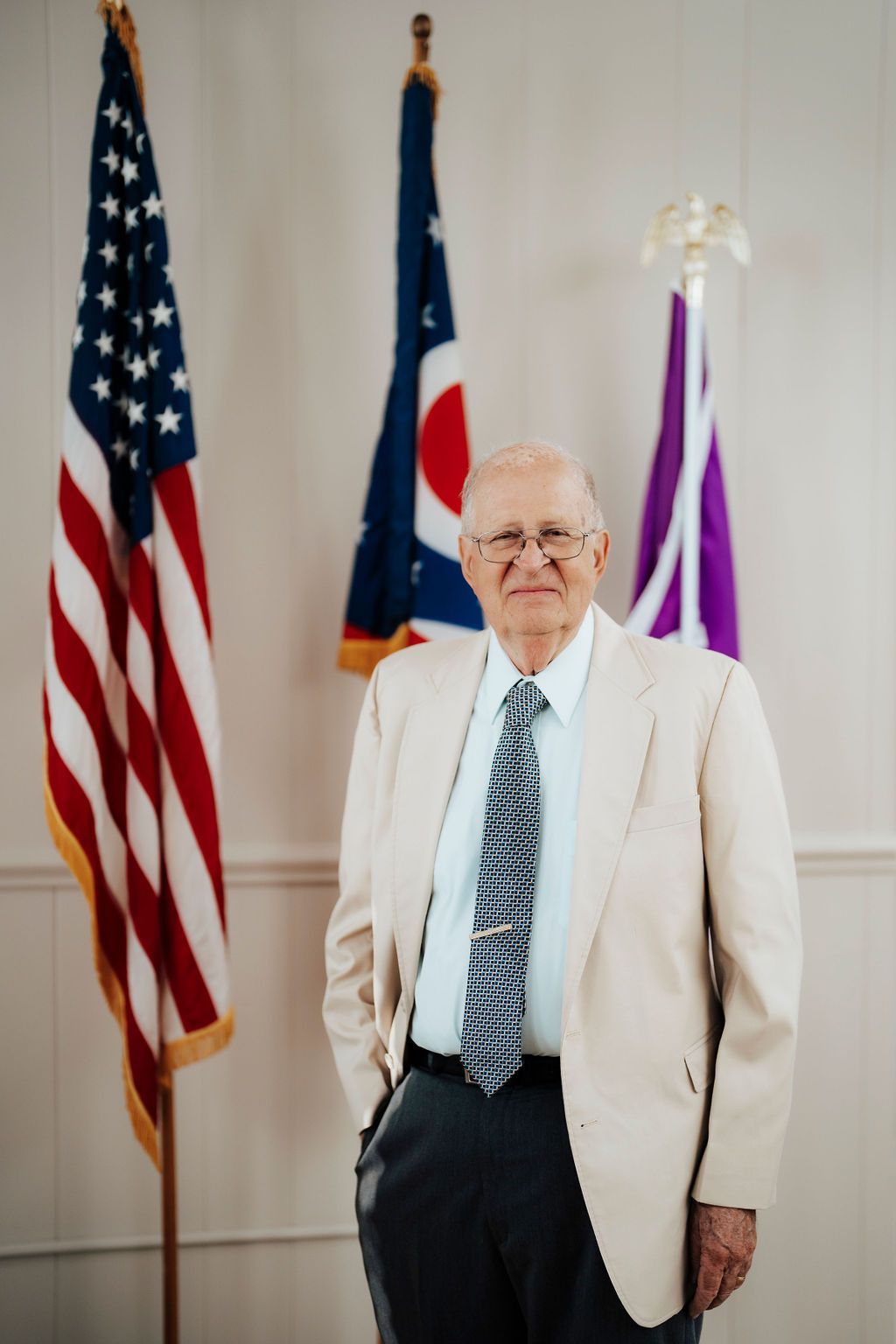 A man in a suit and tie is standing in front of three flags.